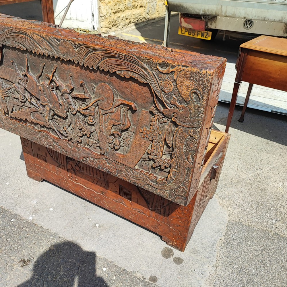 A relief-carved camphor wood trunk with relief panel depictions of figures on horseback and a central brass clasp. View V