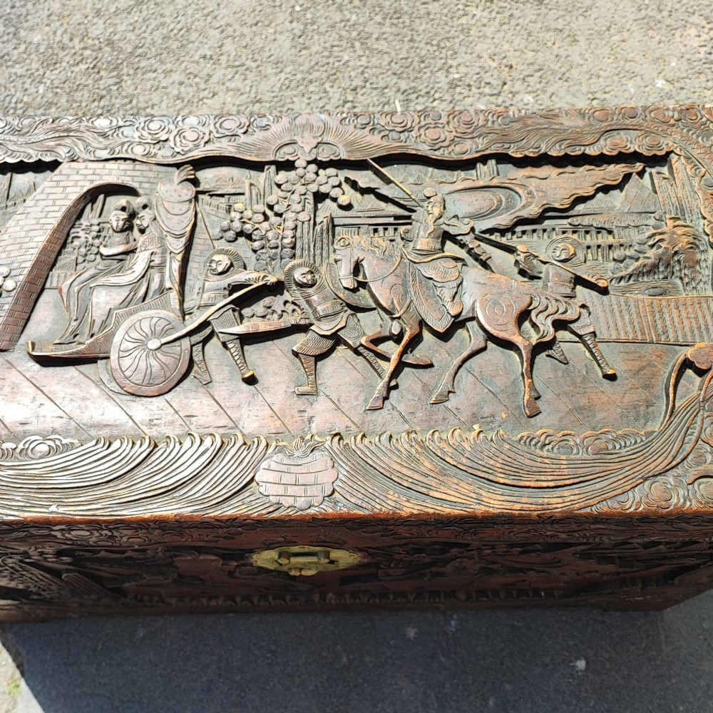A relief-carved camphor wood trunk with relief panel depictions of figures on horseback and a central brass clasp. View VI