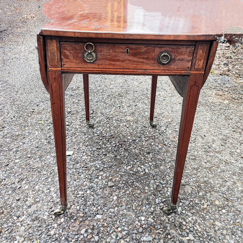 A Georgian mahogany Pembroke table featuring two hinged drop leaves, a central frieze drawer with brass ring handles, boxwood stringing, and tapered legs on brass castors. View II