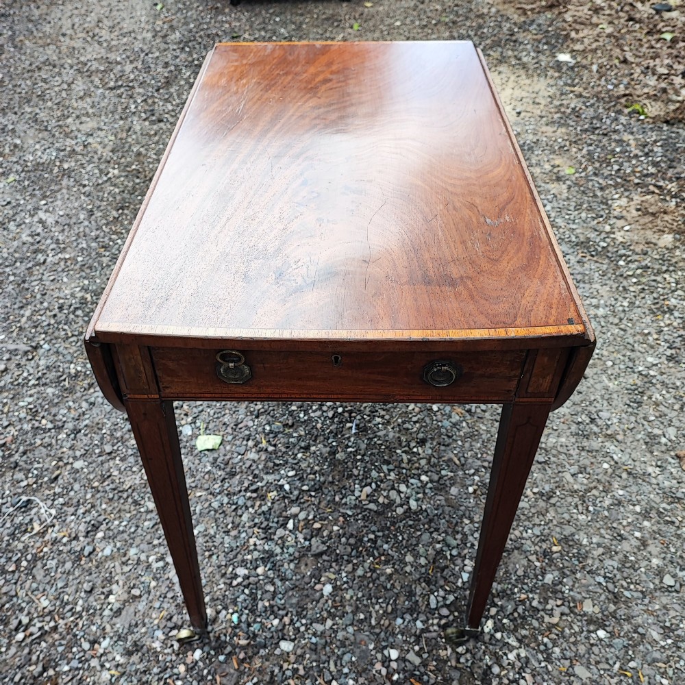 A Georgian mahogany Pembroke table featuring two hinged drop leaves, a central frieze drawer with brass ring handles, boxwood stringing, and tapered legs on brass castors. View III