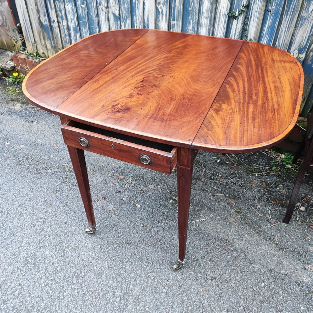 A Georgian mahogany Pembroke table featuring two hinged drop leaves, a central frieze drawer with brass ring handles, boxwood stringing, and tapered legs on brass castors. View IV