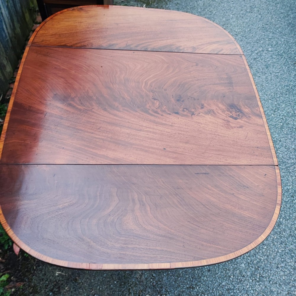 A Georgian mahogany Pembroke table featuring two hinged drop leaves, a central frieze drawer with brass ring handles, boxwood stringing, and tapered legs on brass castors. View VI