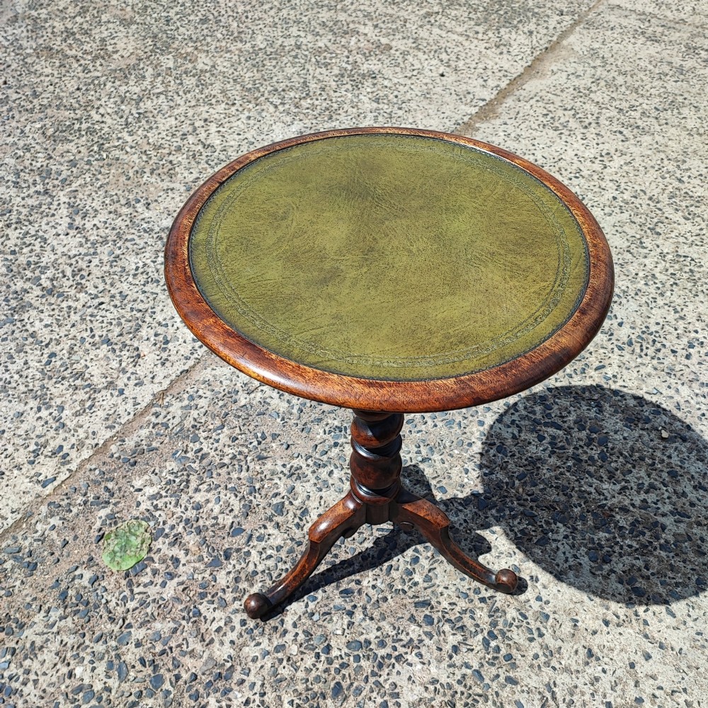 A small circular mahogany wine table with a green leather inset top supported by a turned pedestal column on three cabriole legs.