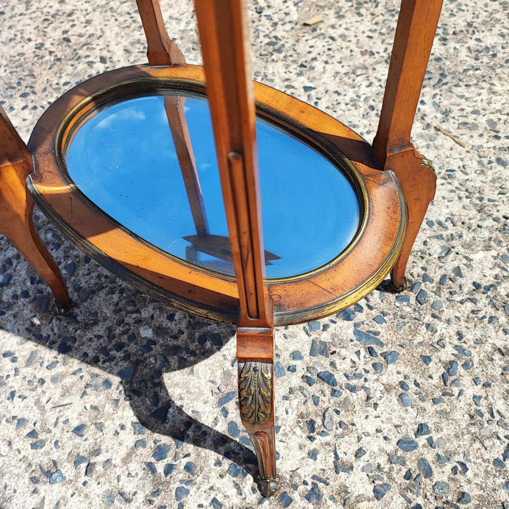 An antique oval satinwood etagere featuring three tiers with glass panels, brass trim, and curved legs adorned with bronze mounts. View VI