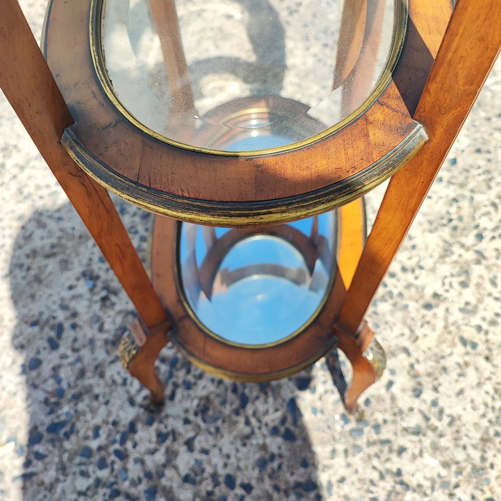 An antique oval satinwood etagere featuring three tiers with glass panels, brass trim, and curved legs adorned with bronze mounts. View VIII