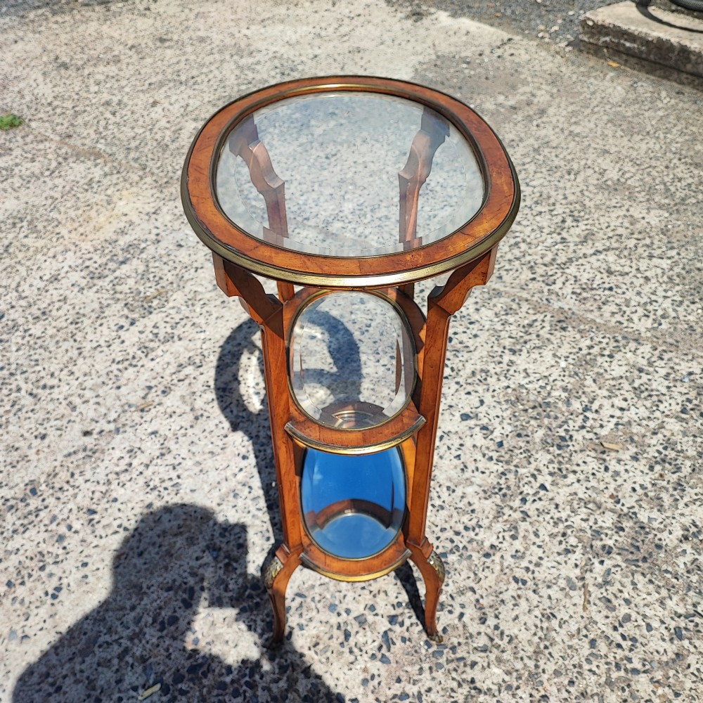 An antique oval satinwood etagere featuring three tiers with glass panels, brass trim, and curved legs adorned with bronze mounts. View IX