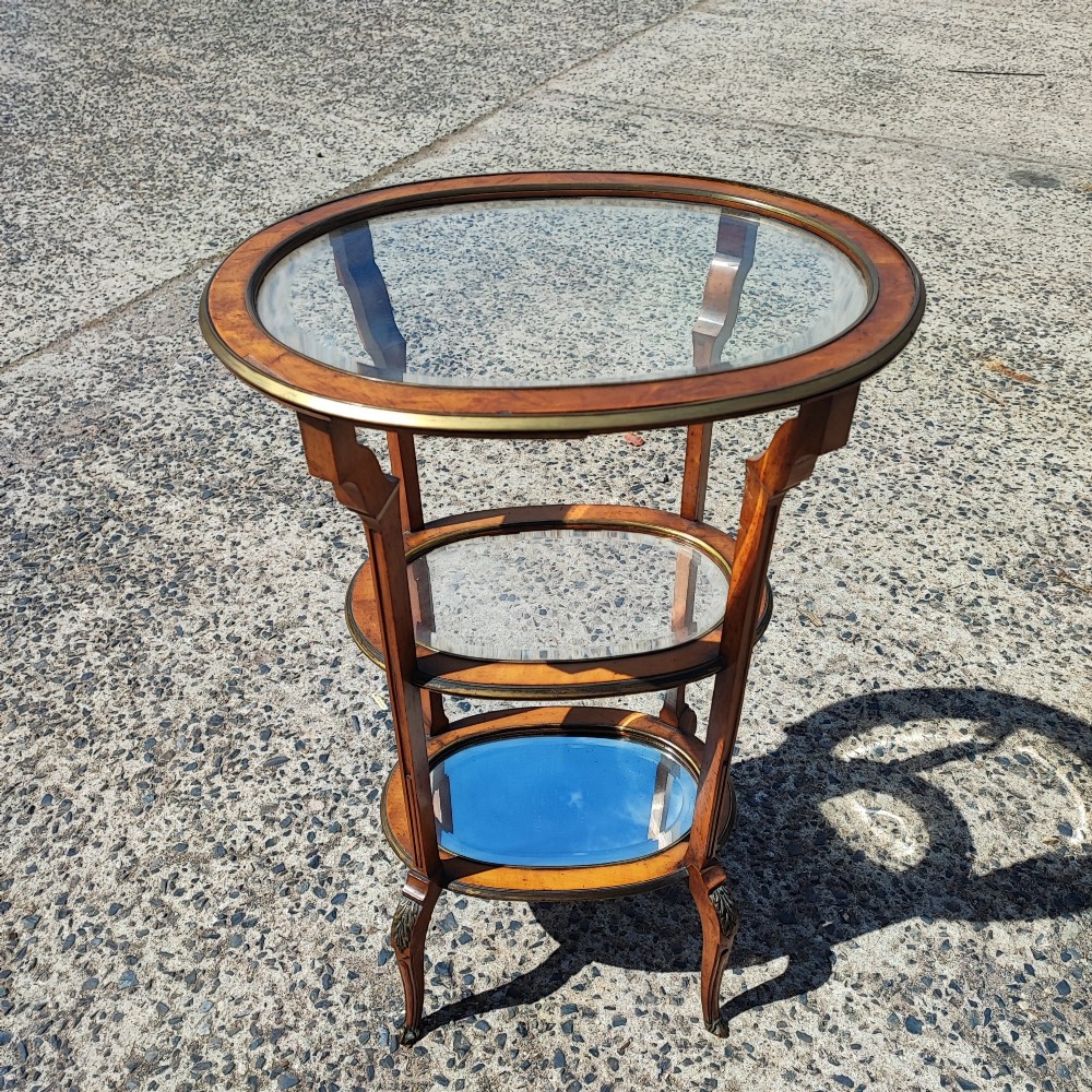 An antique oval satinwood etagere featuring three tiers with glass panels, brass trim, and curved legs adorned with bronze mounts. View XI