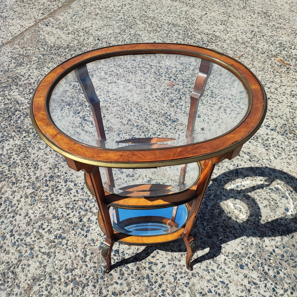 An antique oval satinwood etagere featuring three tiers with glass panels, brass trim, and curved legs adorned with bronze mounts. View XII