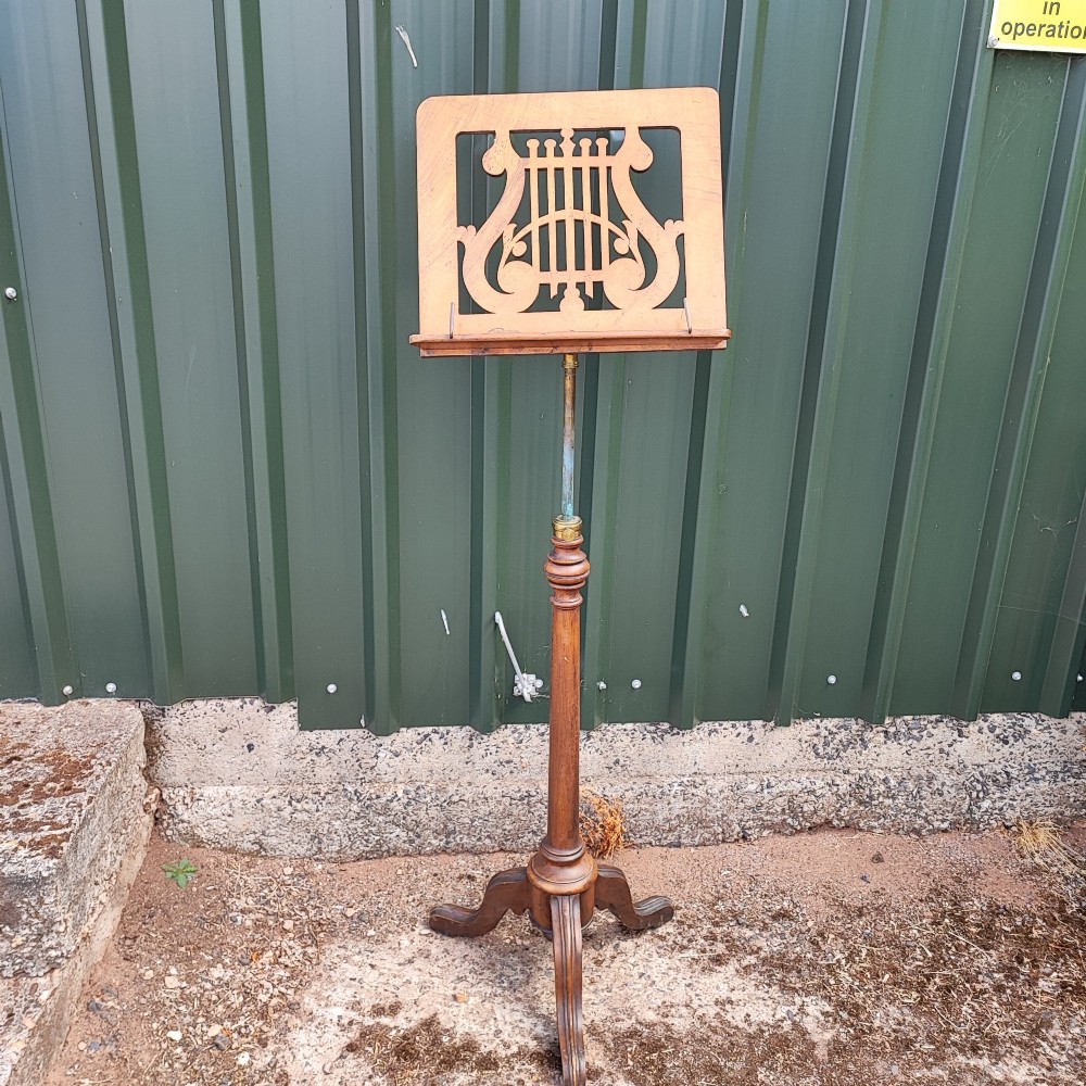 A Victorian walnut music stand featuring a fretwork lyre rest, height-adjustable brass stem, turned column, and carved tripod legs. View VI