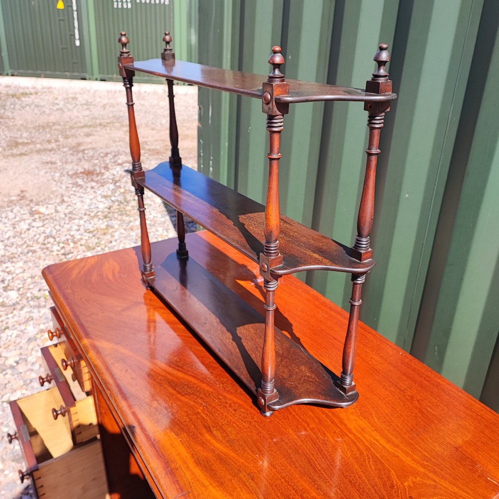 An antique Regency mahogany three-tier hanging shelf with turned spindles and finials.