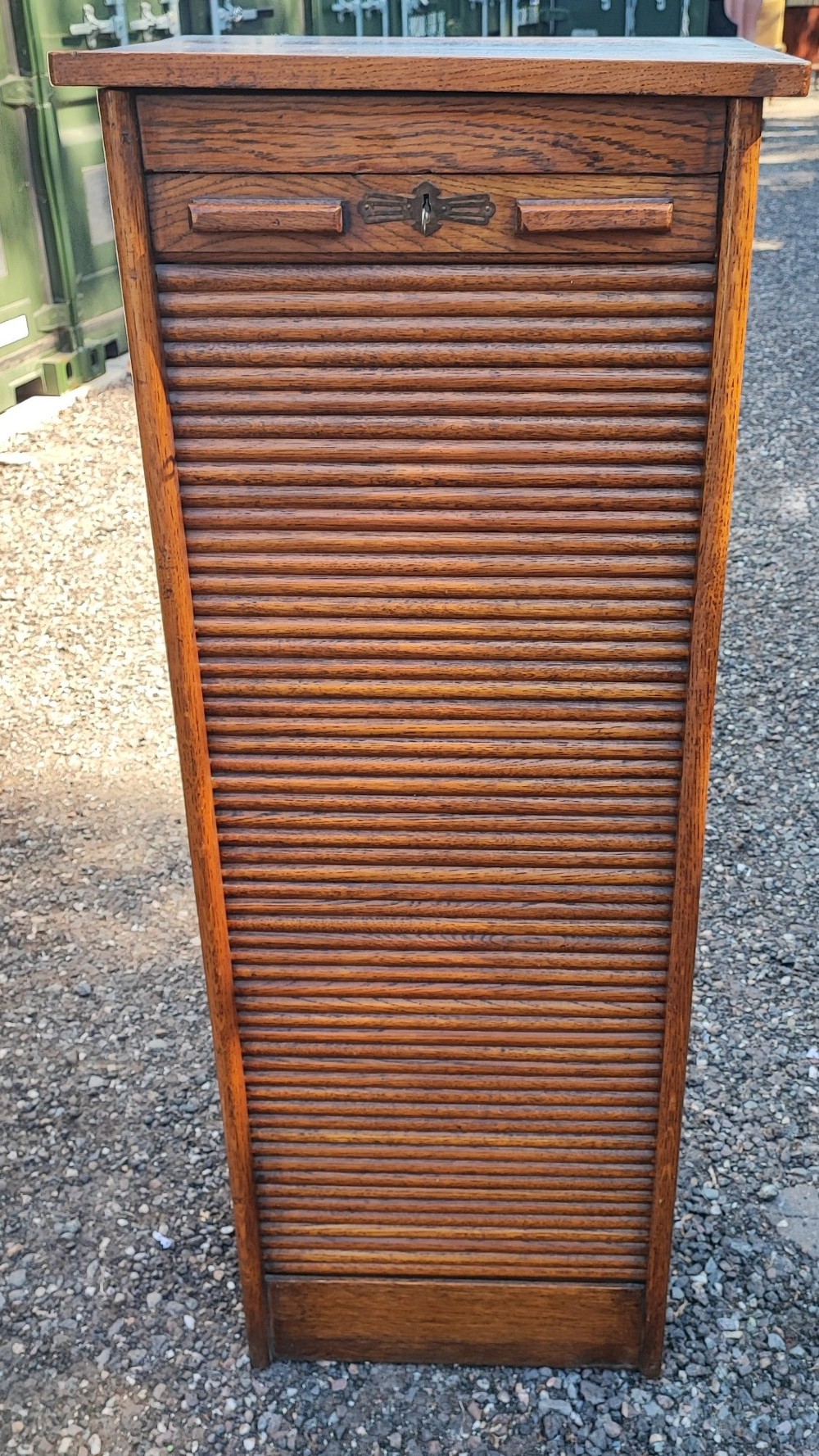 A tall Edwardian oak filing cabinet featuring a slatted wooden tambour front shutter, keyhole escutcheon with key, and wooden pull handles. View II
