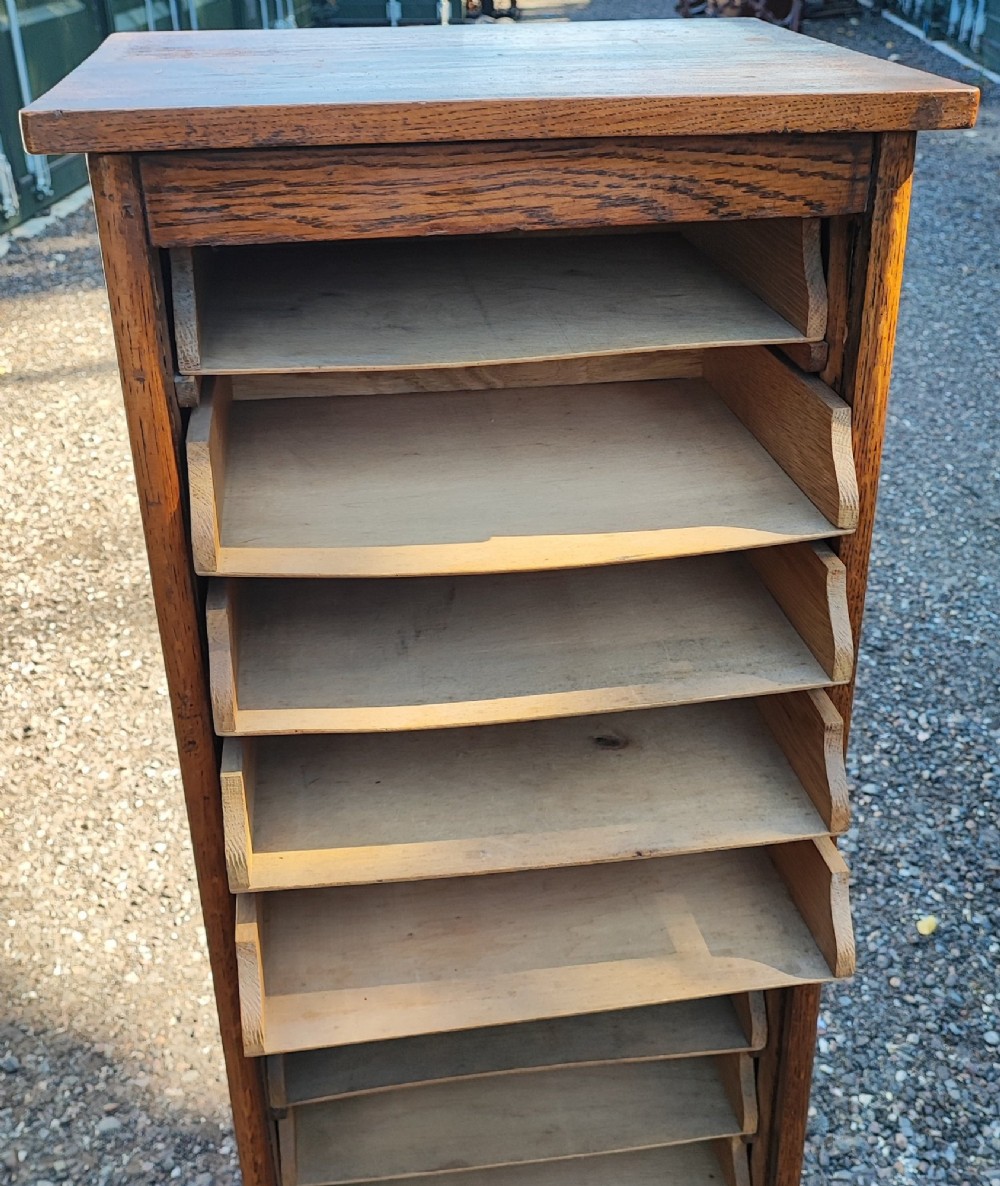 A tall Edwardian oak filing cabinet featuring a slatted wooden tambour front shutter, keyhole escutcheon with key, and wooden pull handles. View IX