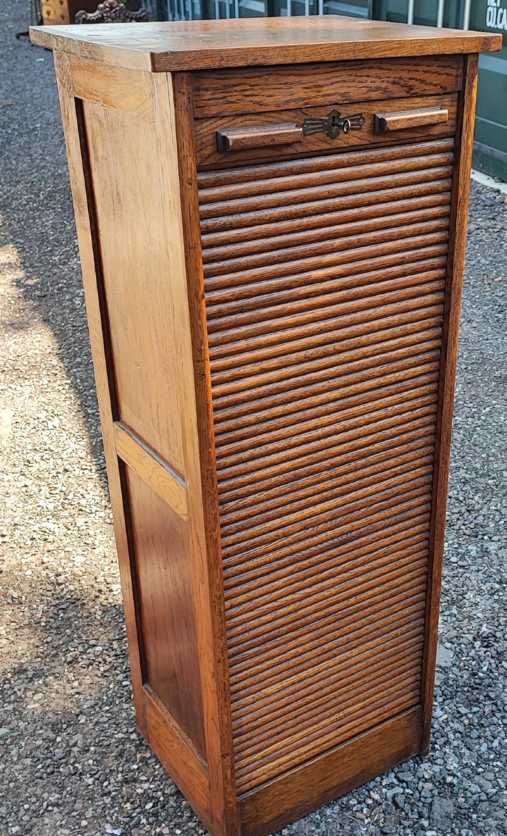 A tall Edwardian oak filing cabinet featuring a slatted wooden tambour front shutter, keyhole escutcheon with key, and wooden pull handles. View XI