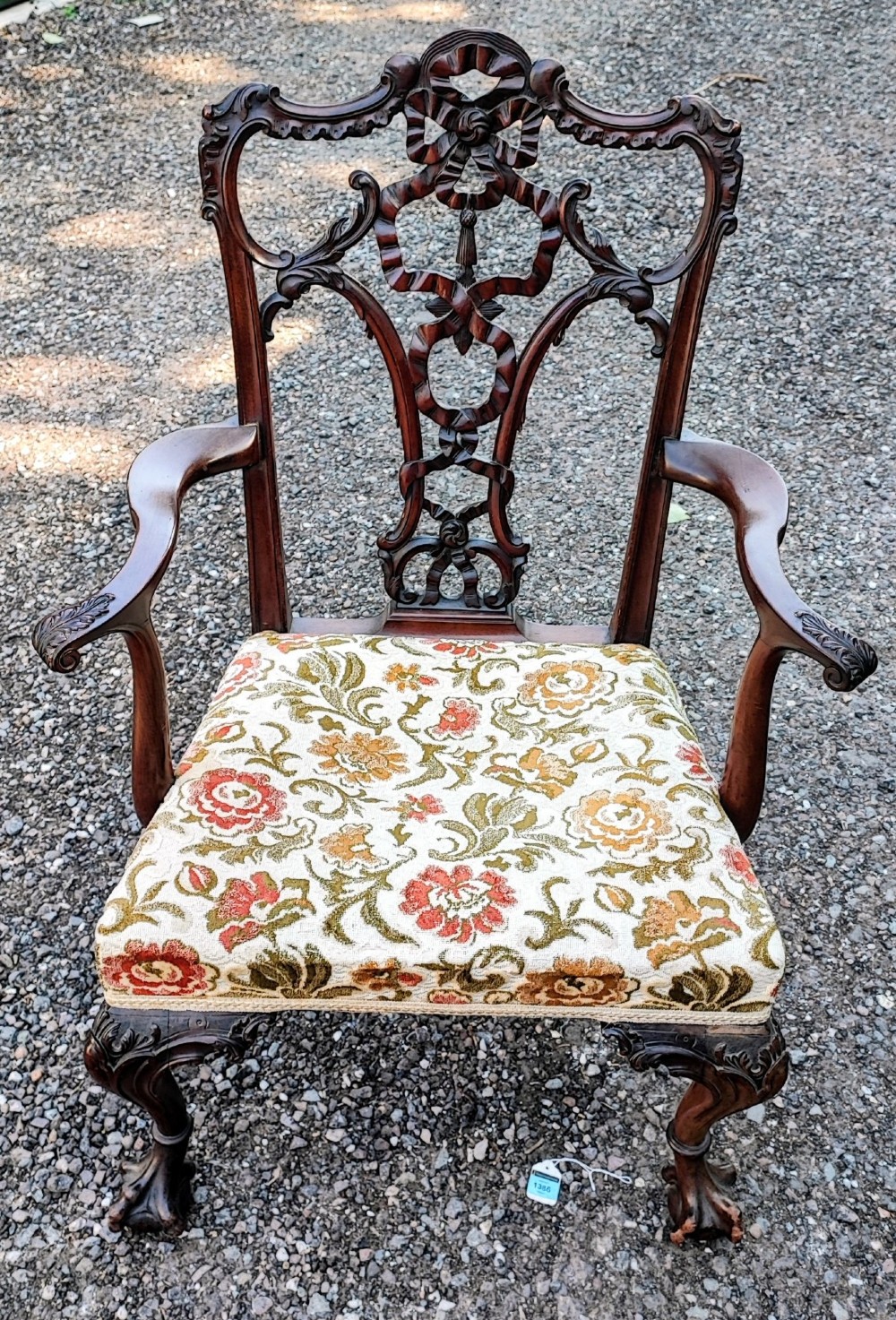 An antique carved mahogany Chippendale style armchair featuring an intricate ribbon-back splat, carved armrests, floral pattern fabric seat, and cabriole legs with ball-and-claw feet. View V