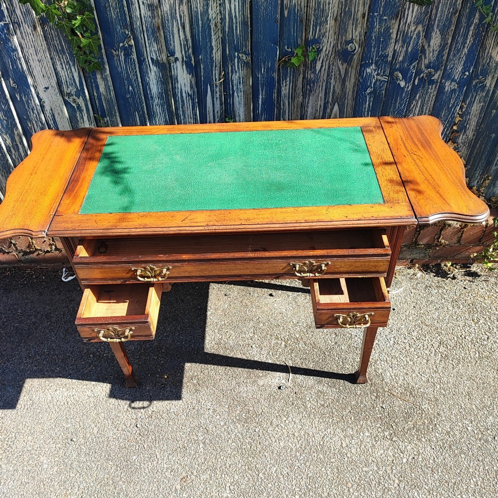 A mahogany drop-leaf writing desk with a green inset writing surface, three drawer handles, and extended side flaps.