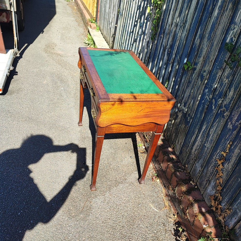 A mahogany drop-leaf writing desk with a green inset writing surface, three drawer handles, and extended side flaps. View II