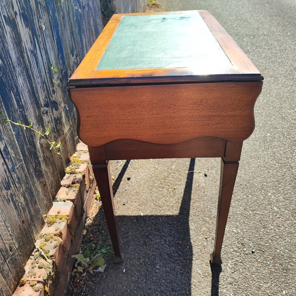 A mahogany drop-leaf writing desk with a green inset writing surface, three drawer handles, and extended side flaps. View VI