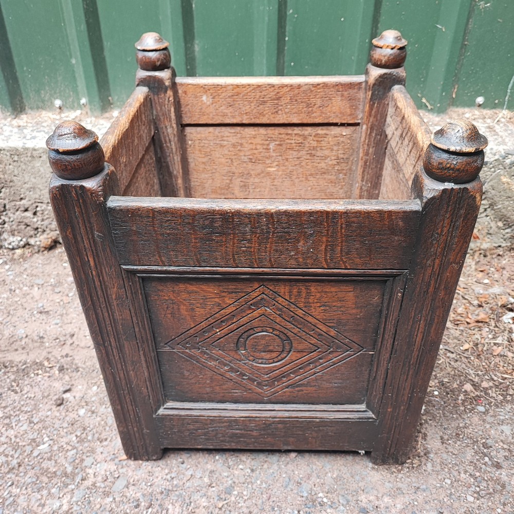 A square dark oak open box featuring carved diamond motifs on the front panel and turned finials atop four corner posts. View II