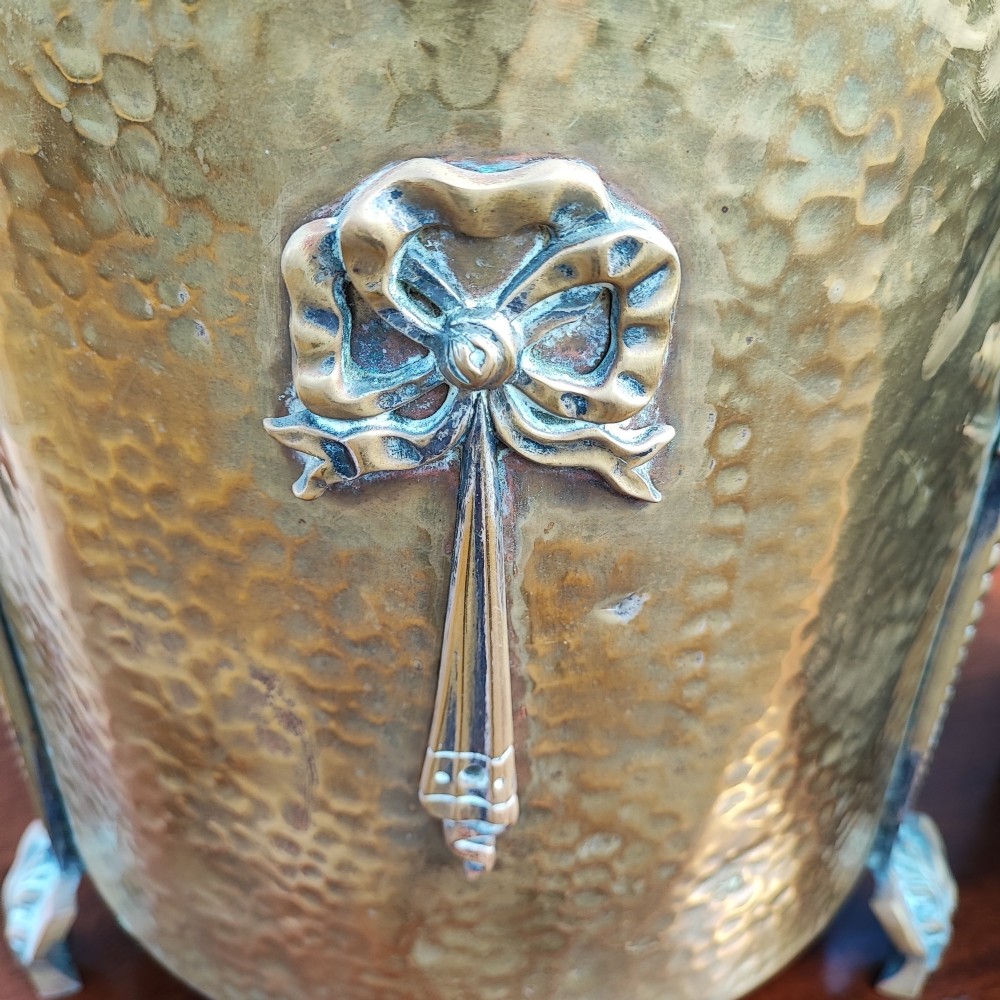 A cylindrical hammered brass coal bin with an acorn finial lid, ribbon bow decoration, paw feet, and a removable galvanised metal liner. View III