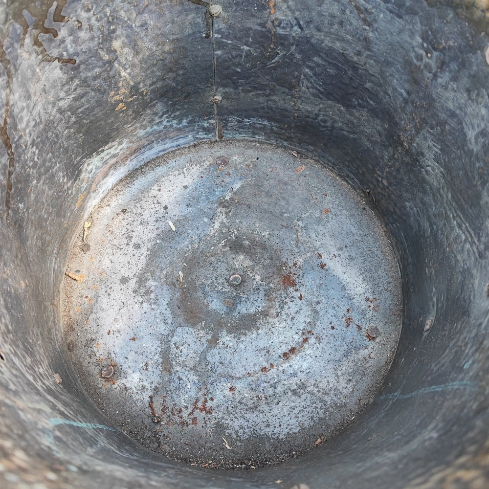 A cylindrical hammered brass coal bin with an acorn finial lid, ribbon bow decoration, paw feet, and a removable galvanised metal liner. View VII