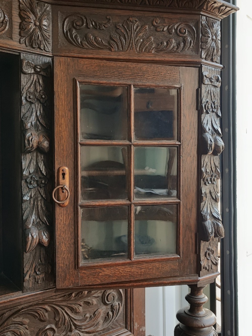 A heavily carved dark oak sideboard featuring a mirrored top section flanked by glazed cabinet doors, resting on turned bulbous supports and a lower shelf. View IV