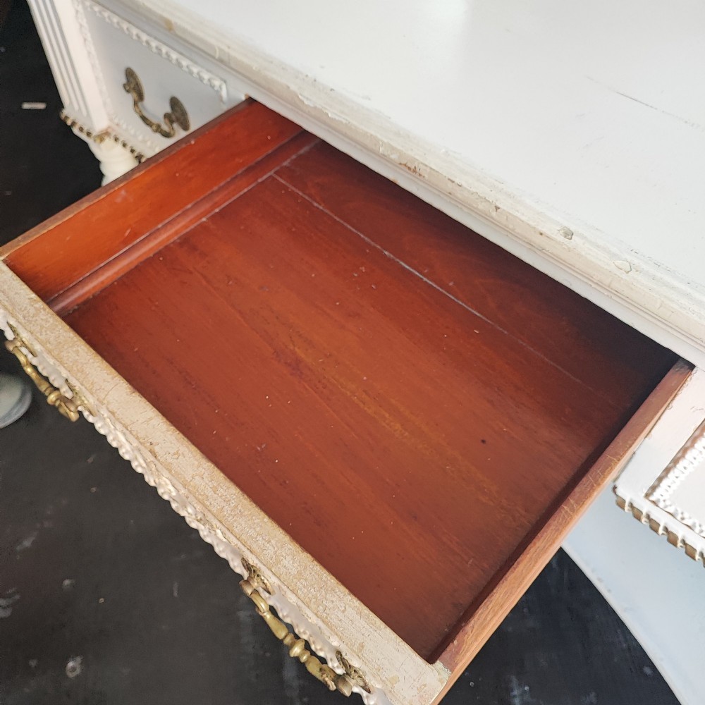 An off-white painted antique dressing table featuring a central triptych mirror, carved gilt details, three drawers with brass handles, and fluted legs on castors. View VII