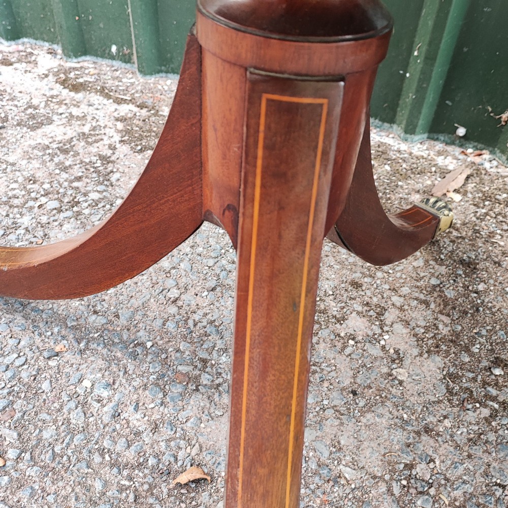 A warm mahogany twin pedestal dining table featuring an oval crossbanded top with string inlay and splayed legs resting on brass claw castors. View IV