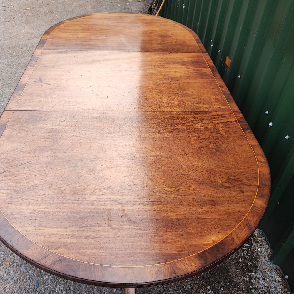 A warm mahogany twin pedestal dining table featuring an oval crossbanded top with string inlay and splayed legs resting on brass claw castors. View VIII