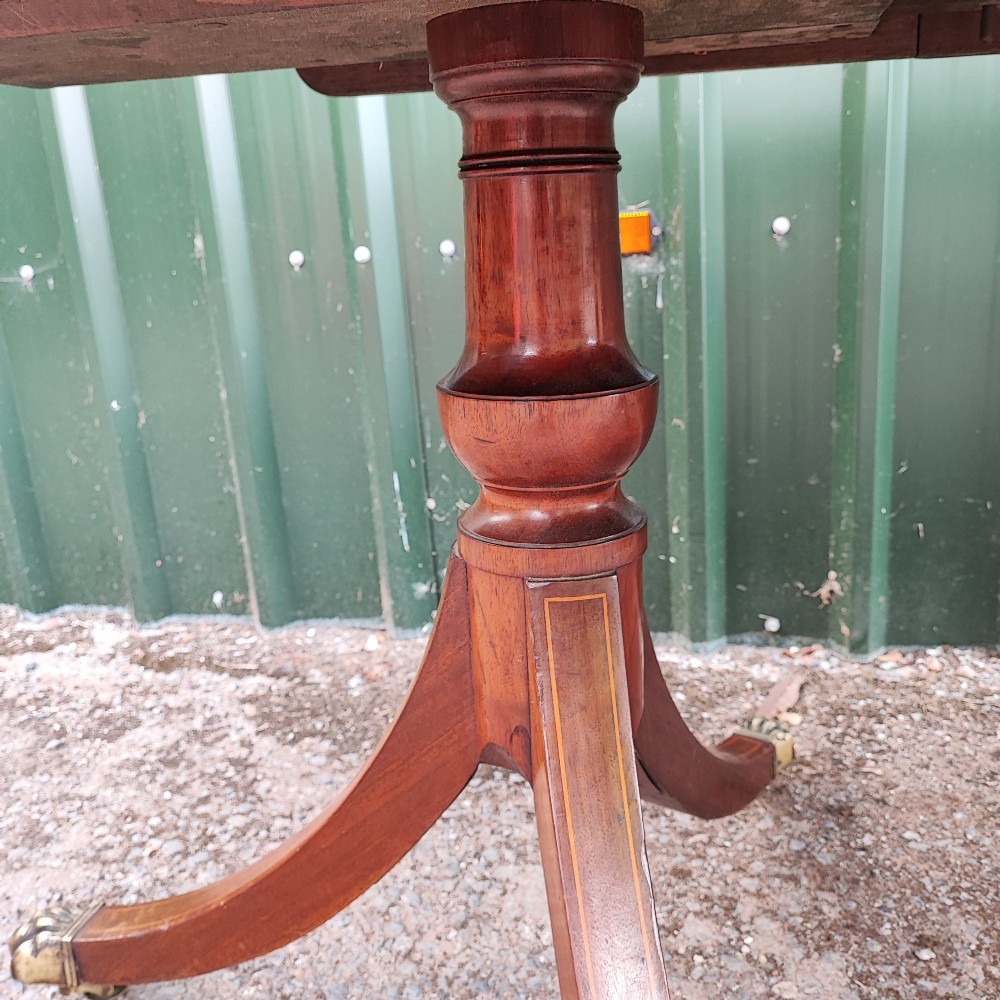 A warm mahogany twin pedestal dining table featuring an oval crossbanded top with string inlay and splayed legs resting on brass claw castors. View IX