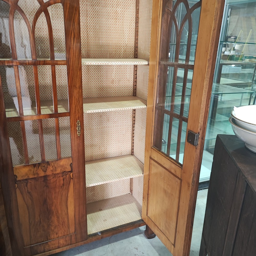 A tall 19th-century walnut display cabinet featuring two glazed doors with Gothic arched tracery above solid figured wood lower panels. View IV
