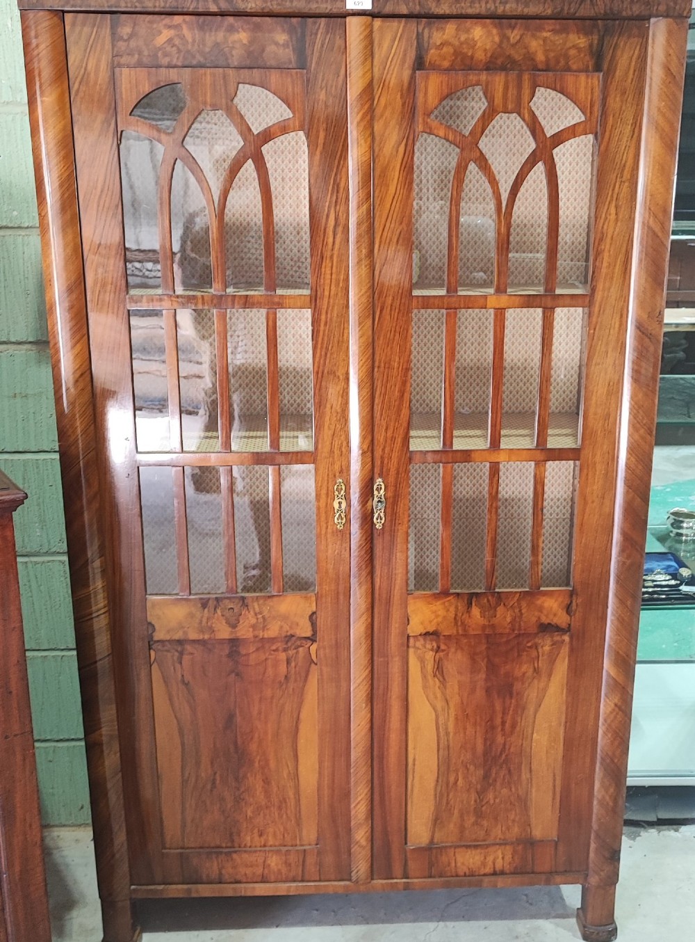 A tall 19th-century walnut display cabinet featuring two glazed doors with Gothic arched tracery above solid figured wood lower panels. View VI