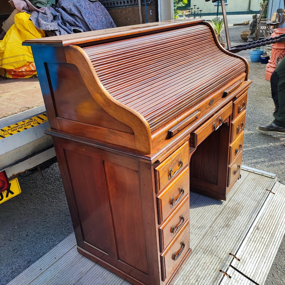 An antique mahogany roll top desk featuring a curved tambour front shutter, twin pedestals with multiple drawers, and brass pull handles. View II