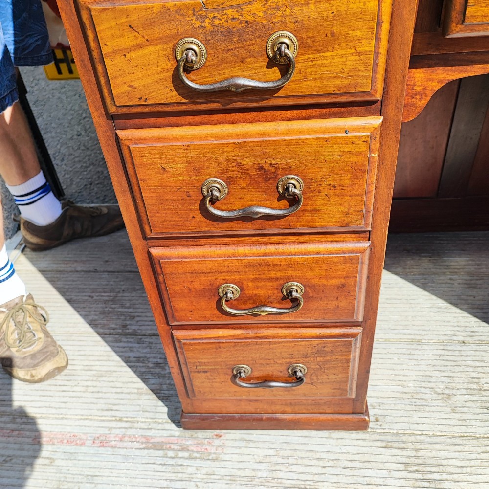 An antique mahogany roll top desk featuring a curved tambour front shutter, twin pedestals with multiple drawers, and brass pull handles. View V