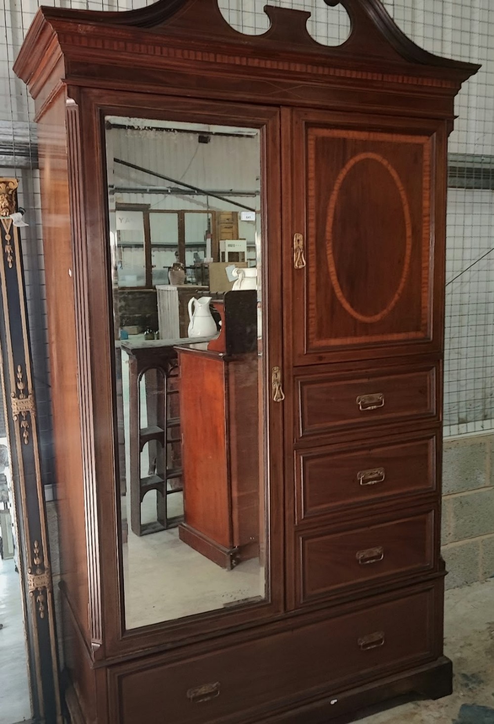 A Victorian mahogany compactum wardrobe featuring a full-length mirrored door on the left alongside a top cupboard with an oval satinwood medallion and several drawers on the right.