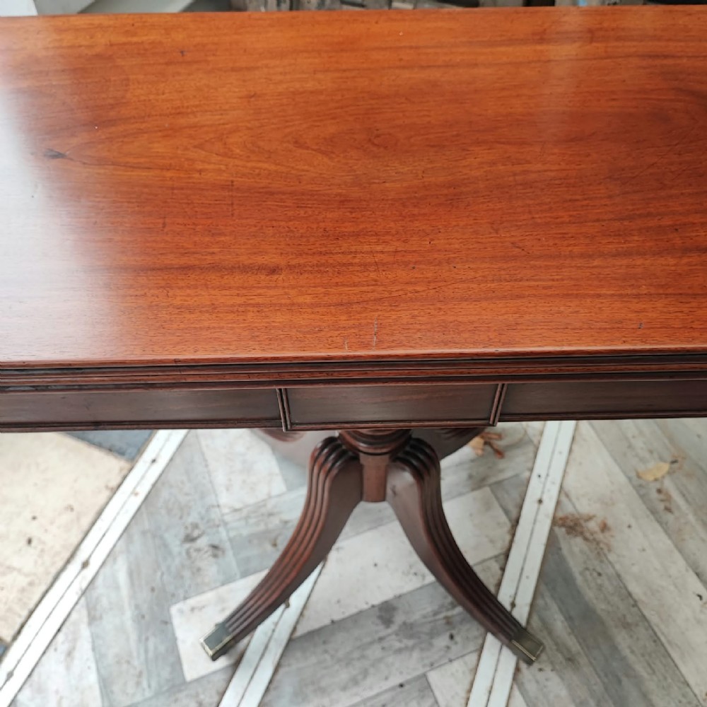 A Regency period mahogany tea table featuring a fold-over polished top, a central pedestal base, and four reeded sabre legs with brass feet. View II