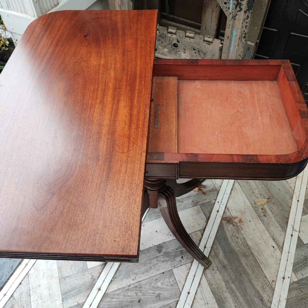 A Regency period mahogany tea table featuring a fold-over polished top, a central pedestal base, and four reeded sabre legs with brass feet. View III