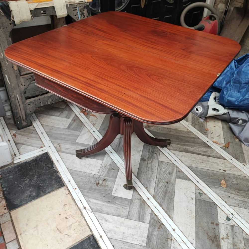 A Regency period mahogany tea table featuring a fold-over polished top, a central pedestal base, and four reeded sabre legs with brass feet. View IV