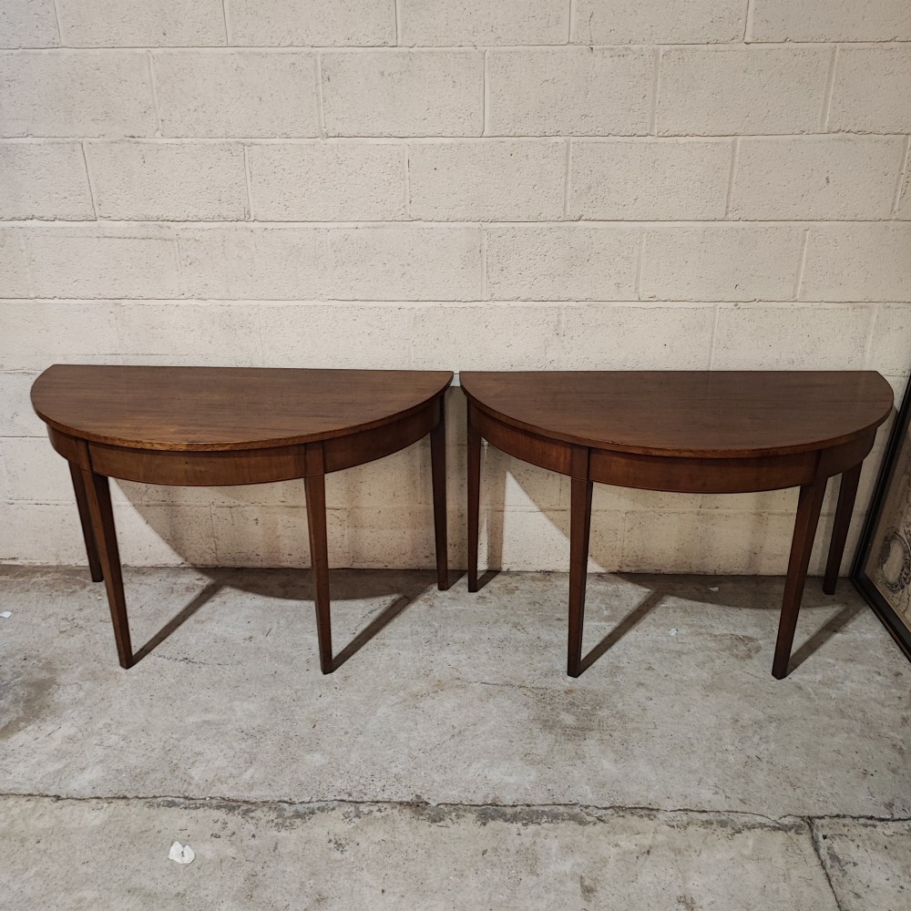 A pair of antique Georgian mahogany demi-lune console tables featuring semi-circular tops and straight tapered legs.