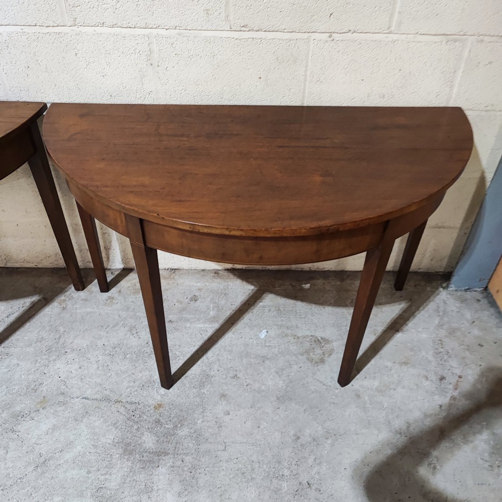 A pair of antique Georgian mahogany demi-lune console tables featuring semi-circular tops and straight tapered legs. View II