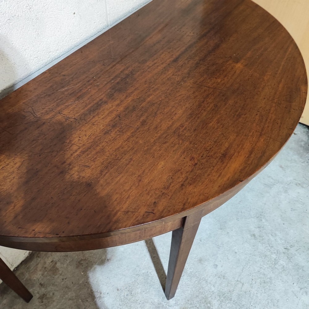 A pair of antique Georgian mahogany demi-lune console tables featuring semi-circular tops and straight tapered legs. View IV