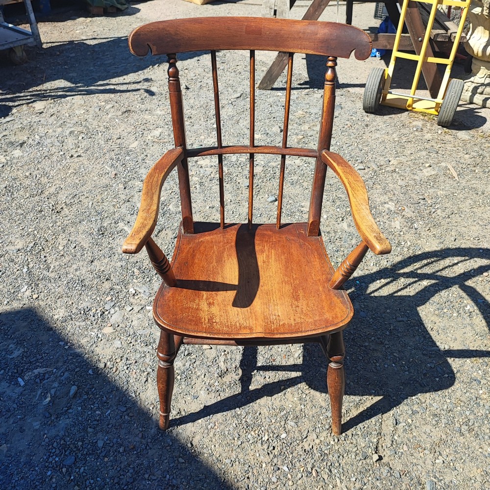 An antique wooden country armchair featuring turned front legs, a spindle backrest with a carved top rail, and curved armrests.