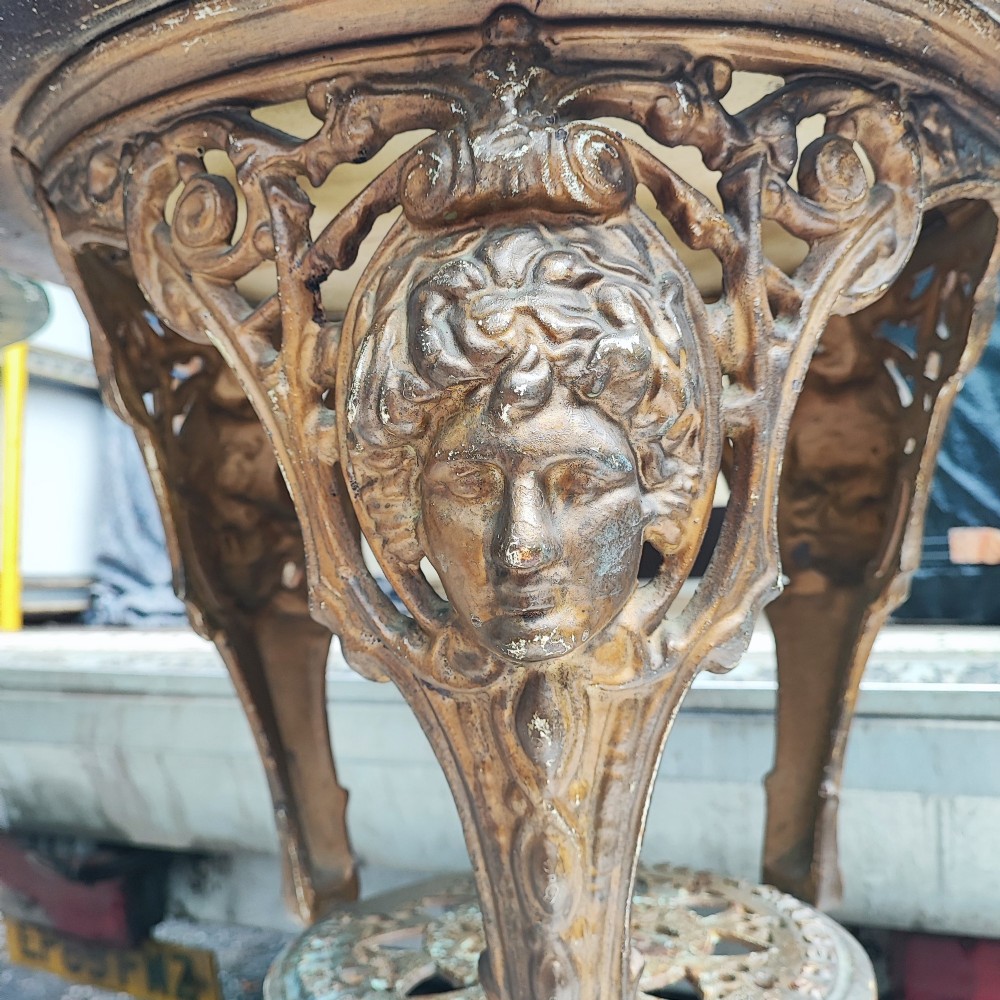 A Victorian cast iron tripod pub table featuring ornate leg castings with classical face motifs, a pierced lower circular tier, and a round wooden tabletop. View VII