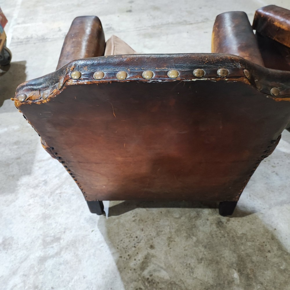A pair of patinated tan brown leather club armchairs featuring shaped backrests, brass studding along the trim, brown velvet seat cushions, and short carved front legs on brass castors. View II