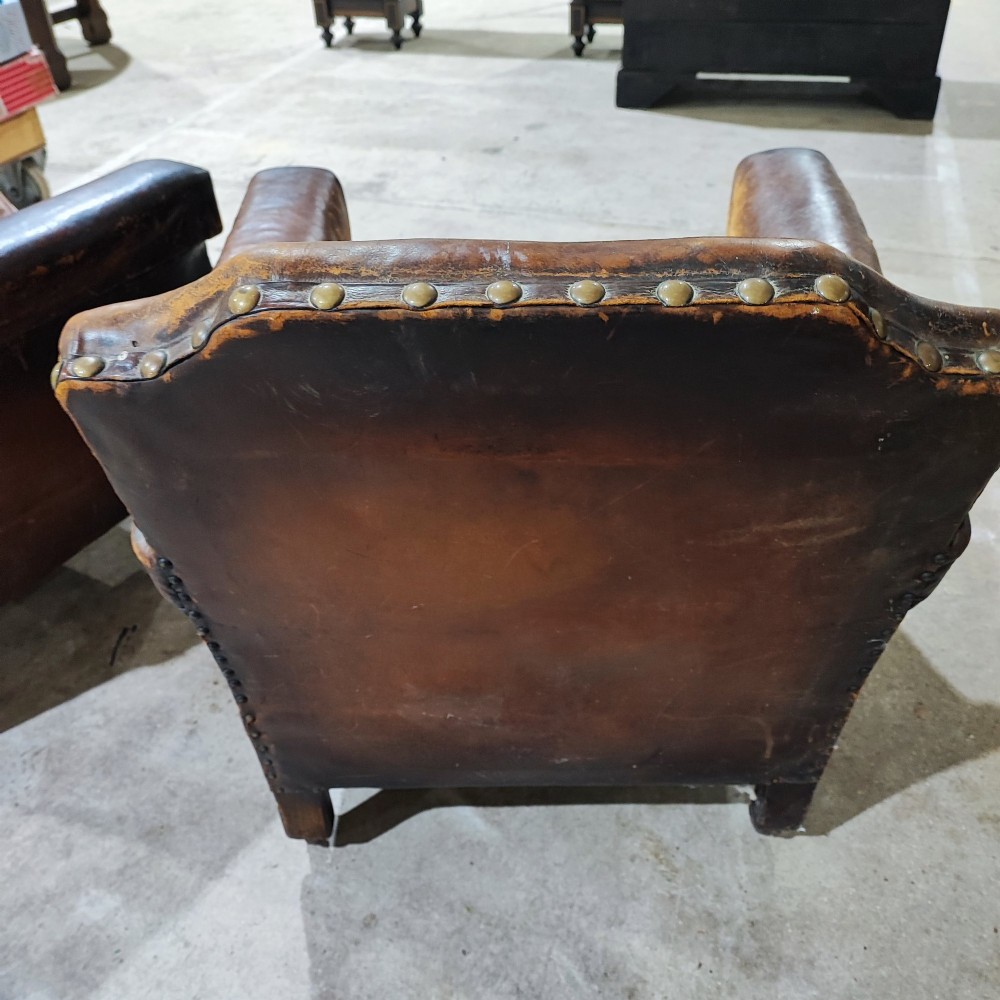 A pair of patinated tan brown leather club armchairs featuring shaped backrests, brass studding along the trim, brown velvet seat cushions, and short carved front legs on brass castors. View III