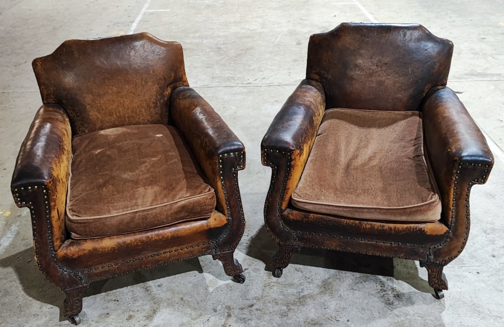 A pair of patinated tan brown leather club armchairs featuring shaped backrests, brass studding along the trim, brown velvet seat cushions, and short carved front legs on brass castors. View VIII