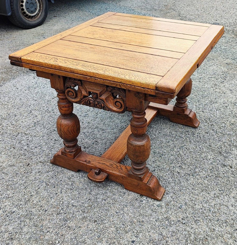 A solid oak refectory dining table featuring a draw-leaf extension mechanism, carved apron, turned baluster legs, and a low central stretcher base. View II