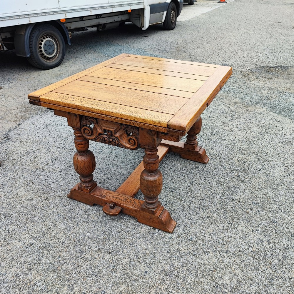 A solid oak refectory dining table featuring a draw-leaf extension mechanism, carved apron, turned baluster legs, and a low central stretcher base. View III