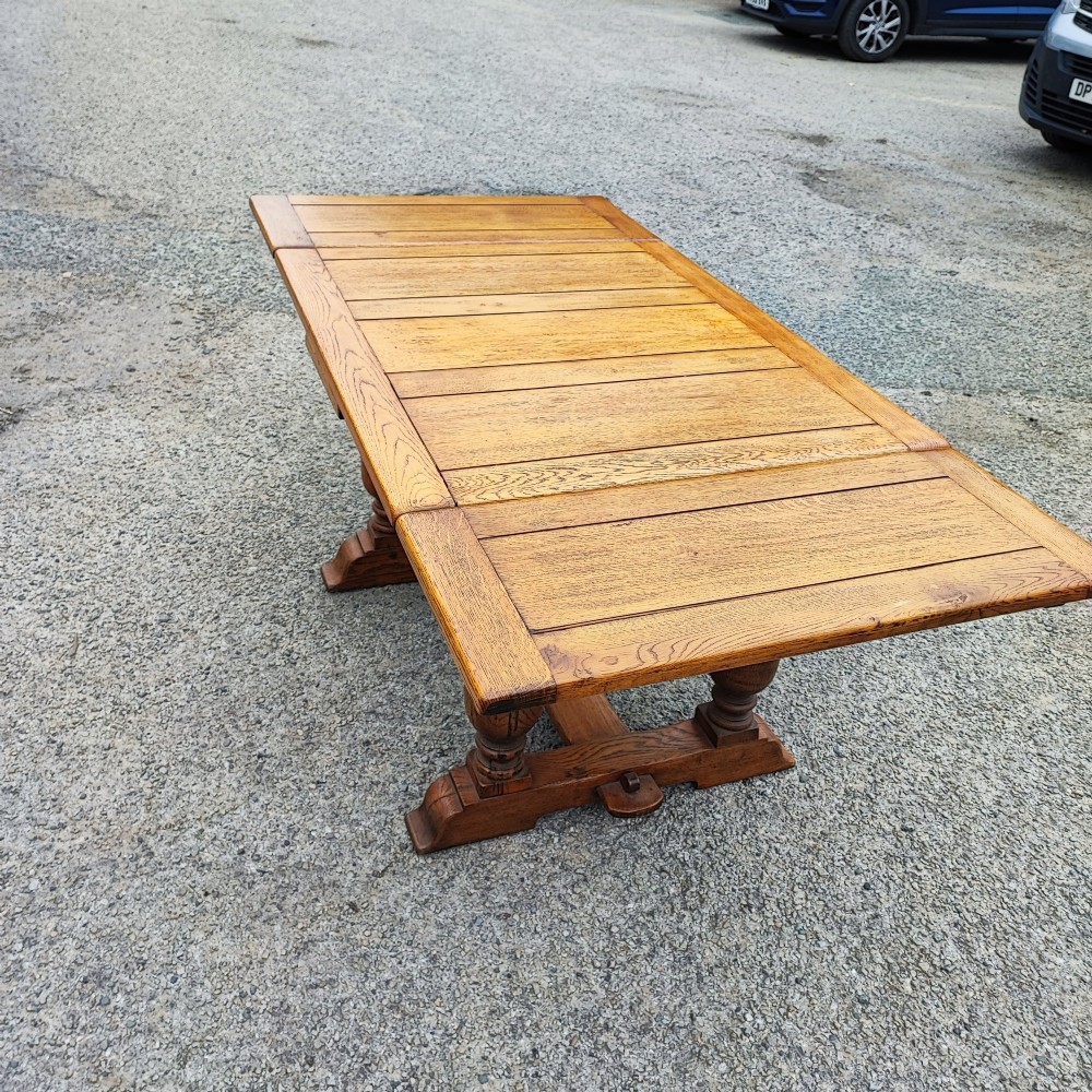 A solid oak refectory dining table featuring a draw-leaf extension mechanism, carved apron, turned baluster legs, and a low central stretcher base. View VI