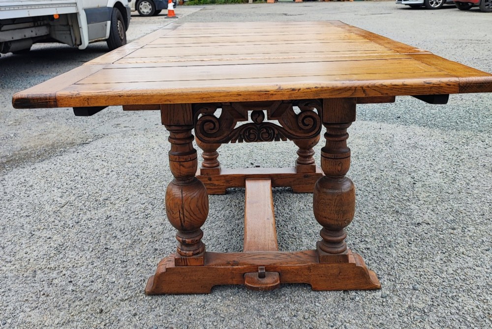 A solid oak refectory dining table featuring a draw-leaf extension mechanism, carved apron, turned baluster legs, and a low central stretcher base. View IX
