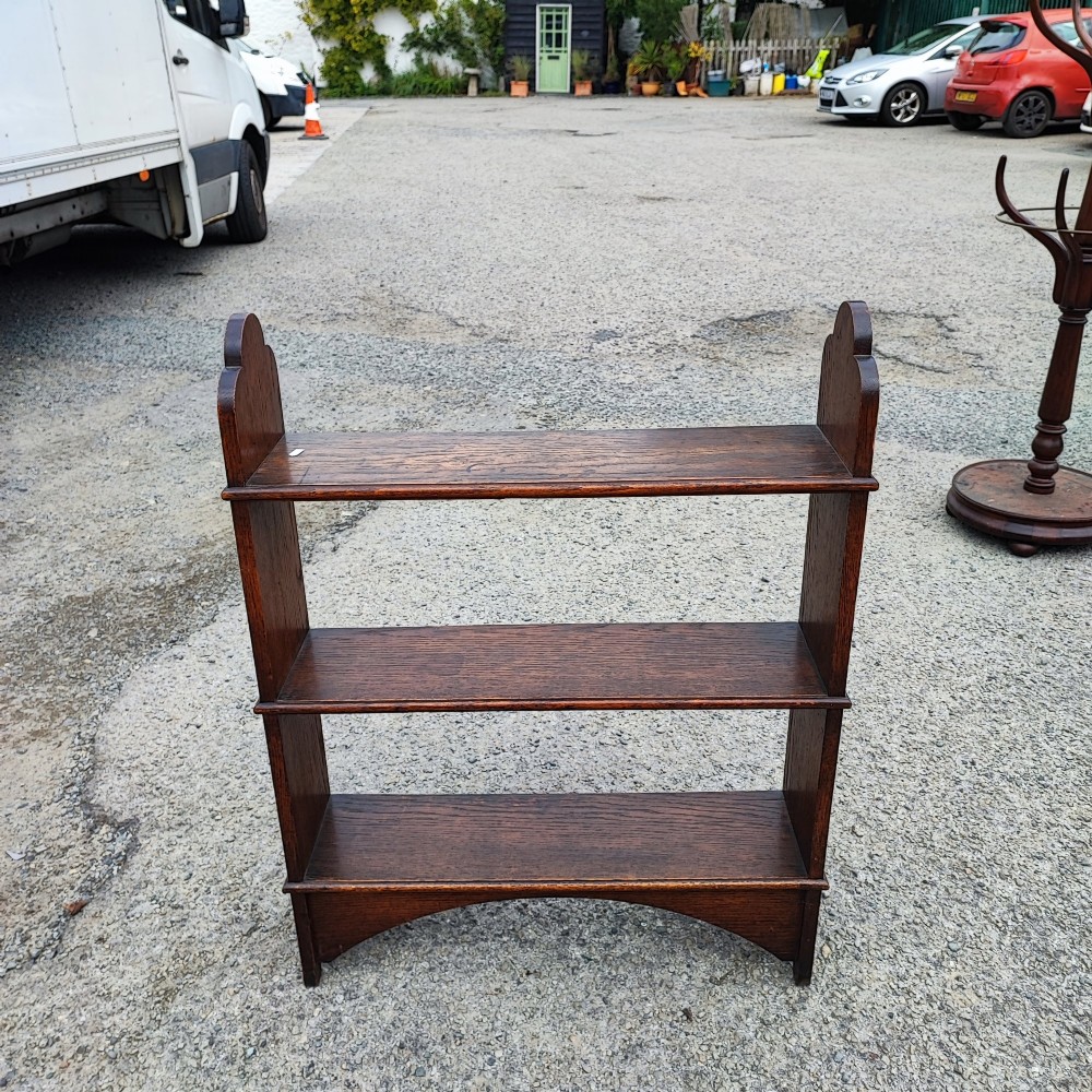 A low three-tier open oak bookcase featuring shaped side uprights and an arched apron base. View III
